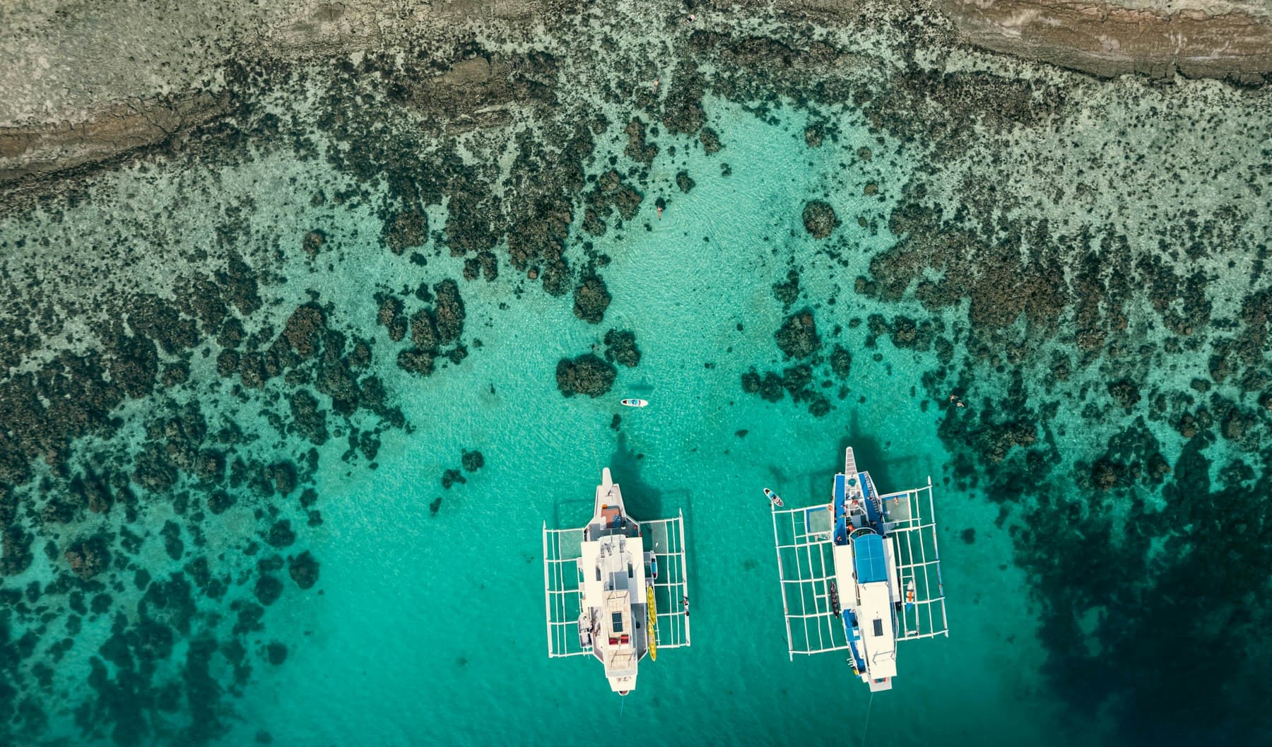 Small boats anchored in clear turquoise water beside a tropical shoreline