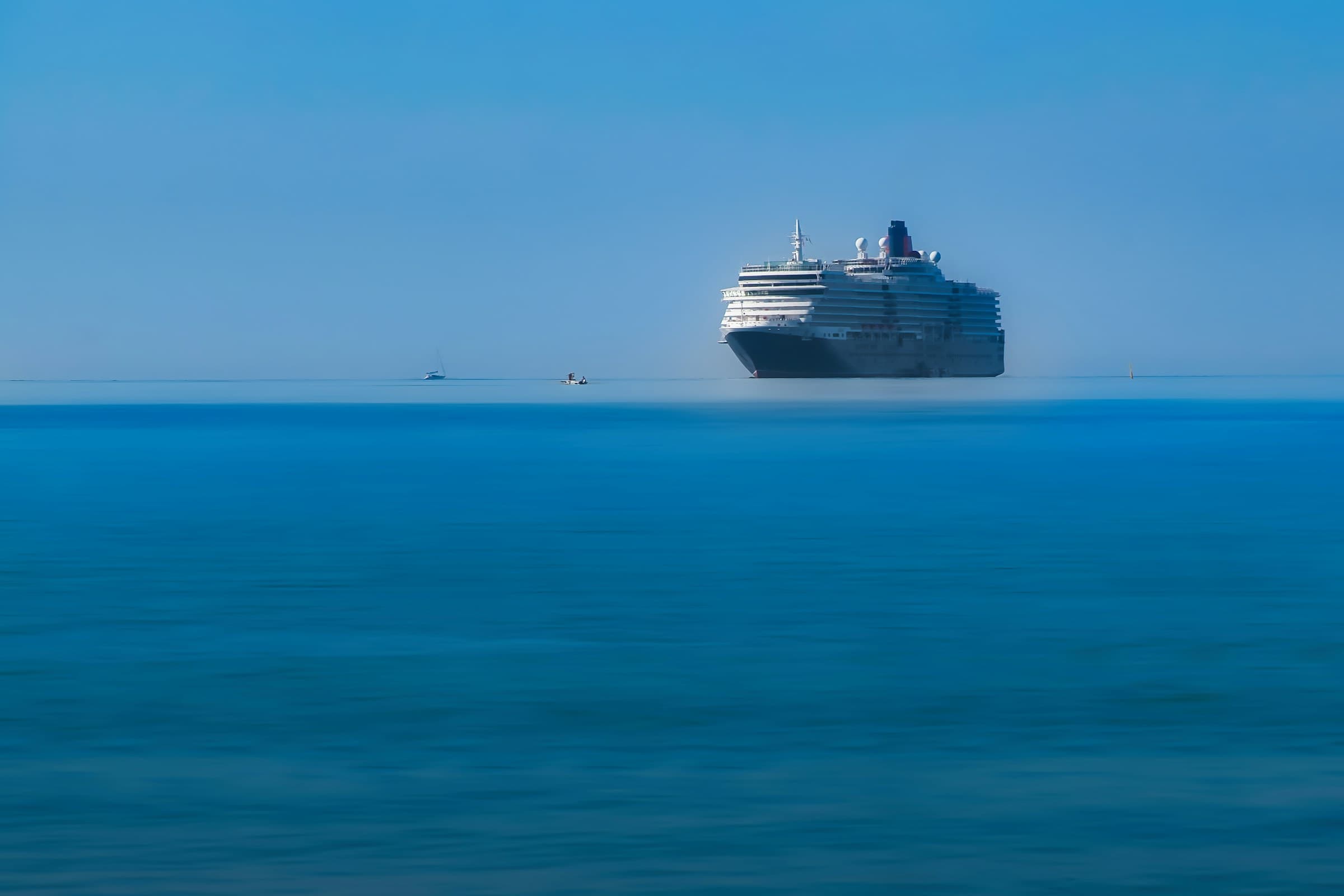 A cruise ship on calm blue water, seen from a distance