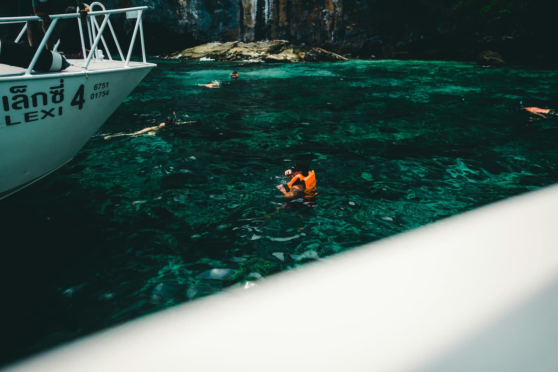 Snorkelers in clear turquoise shallows beside a rocky tropical shore